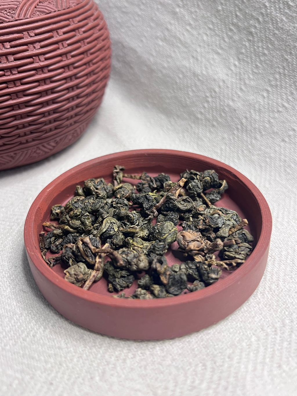 Dark rose woven lacquer tea caddy open beside its lid filled with rolled Da Ye oolong leaves