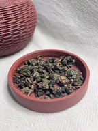 Dark rose woven lacquer tea caddy open beside its lid filled with rolled Da Ye oolong leaves