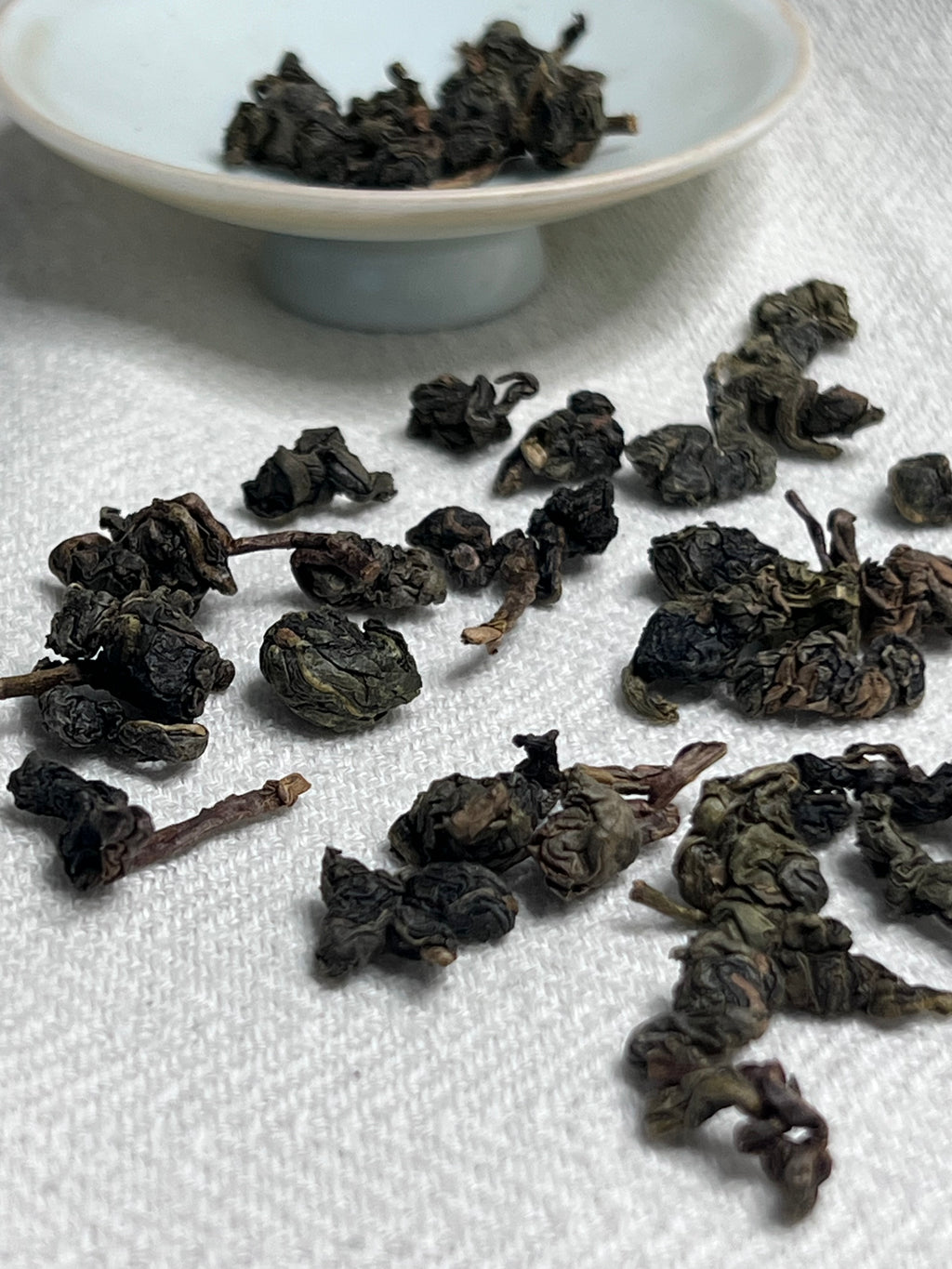 Da Ye Bug-Bitten oolong leaves spread on white linen with a small white ceramic saucer in soft focus