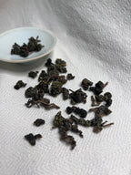 Rolled Da Ye oolong leaves scattered across white linen with a celadon saucer in the background