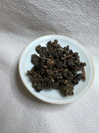 Overhead view of Da Ye Bug-Bitten Oolong leaves mounded in a small white ceramic dish on grey linen